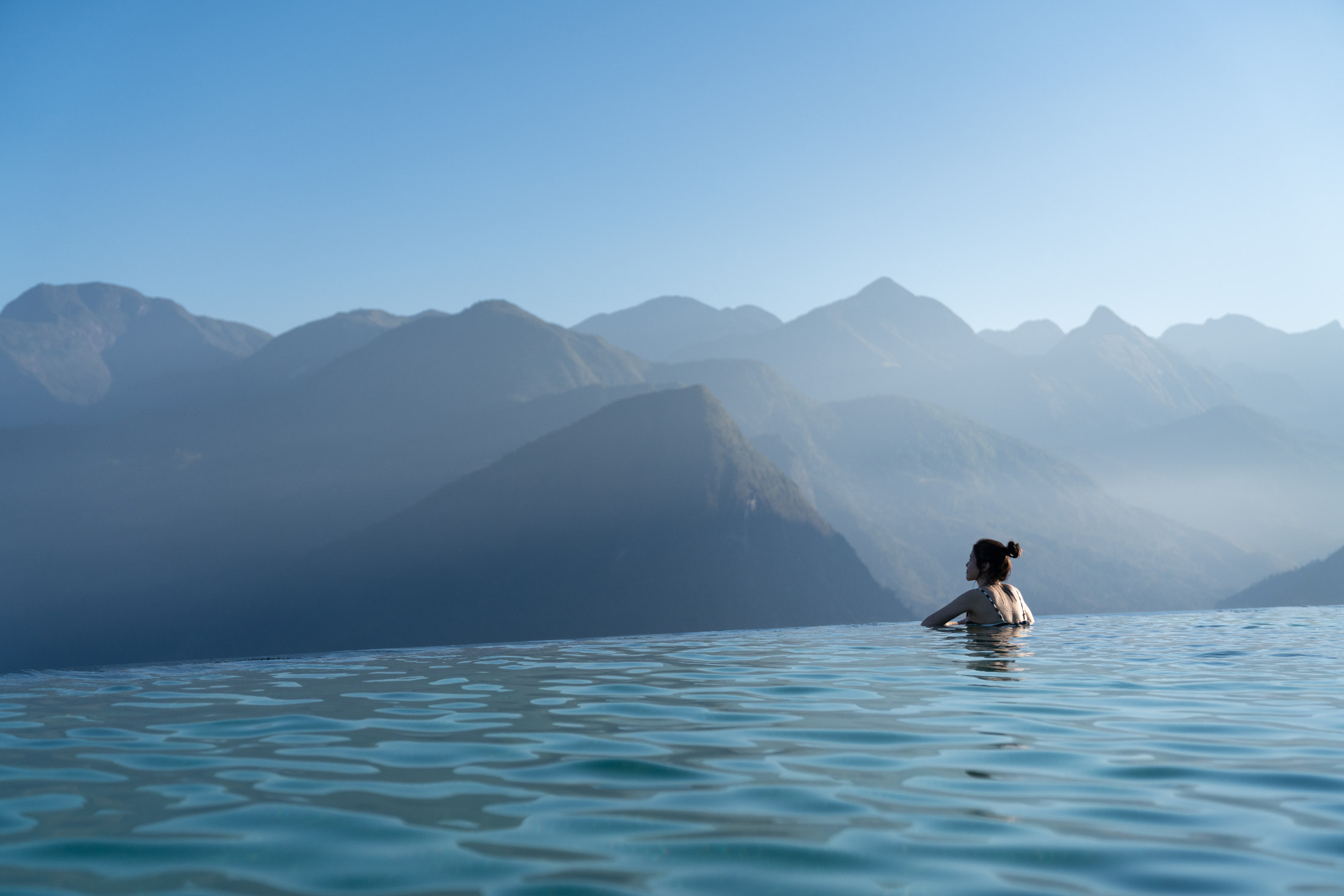 Guest in an infinity pool facing misty mountains